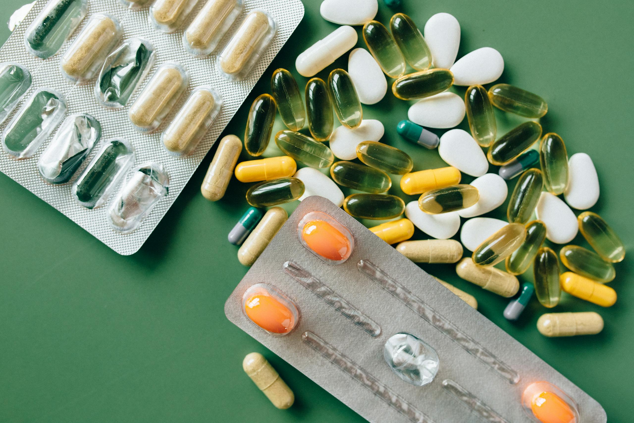 Variety of capsules and tablets laid out on a green surface for healthcare concept.