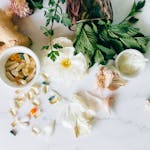 A flatlay of herbal supplements with fresh ginger, garlic, and leaves.