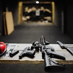 A selection of firearms and safety gear on a table at an indoor shooting range.