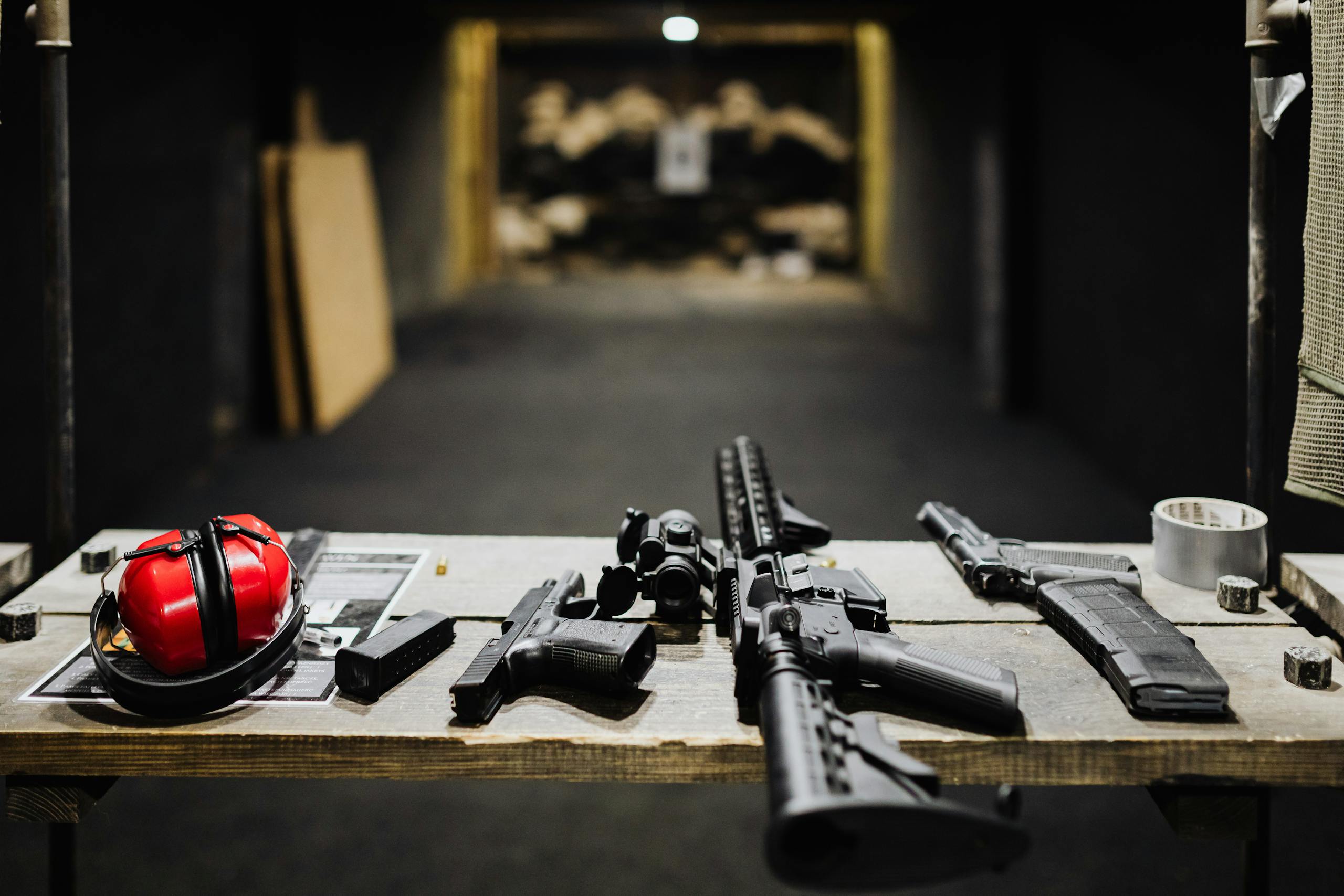 A selection of firearms and safety gear on a table at an indoor shooting range.