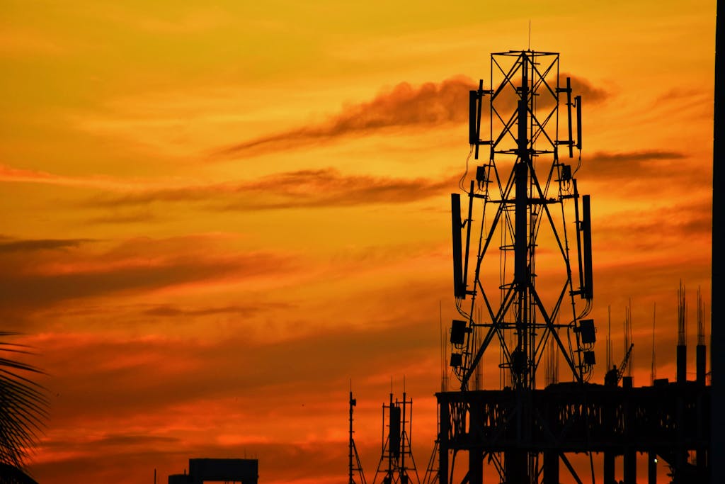 Silhouette of transmission towers against a vibrant orange sunset sky in Mymensingh, Bangladesh.